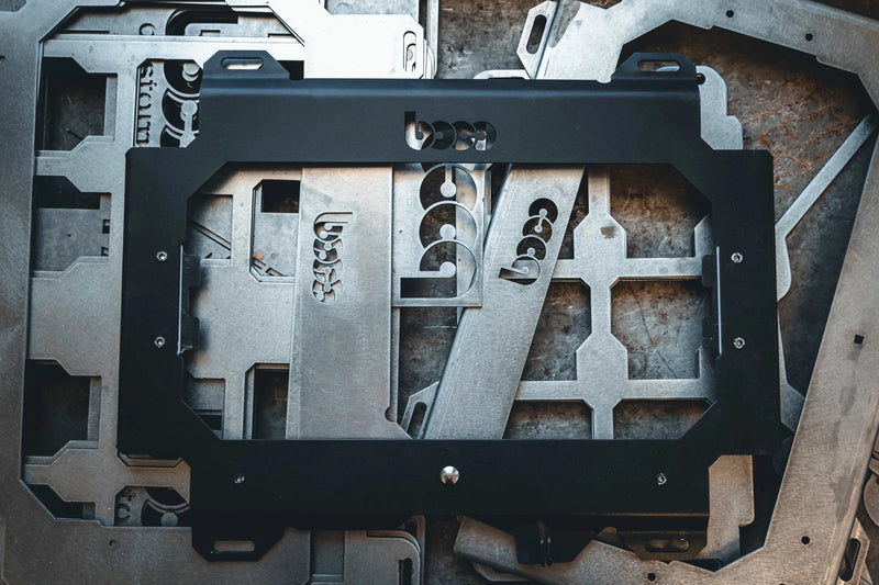 Artistic view of the raw steel Husky Build-Out locking mounting plate alongside shop fabrication materials, highlighting the American-made industrial quality of BOCO Custom mounts.
