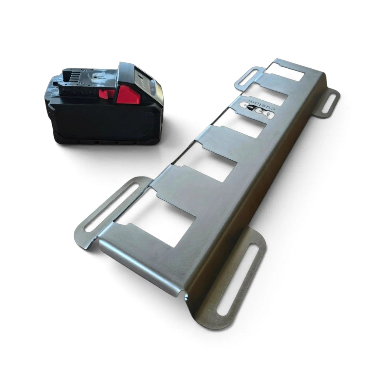 A silver metal mounting bracket with four rectangular cutouts and two looped side tabs, shown on a white background next to a black battery pack.