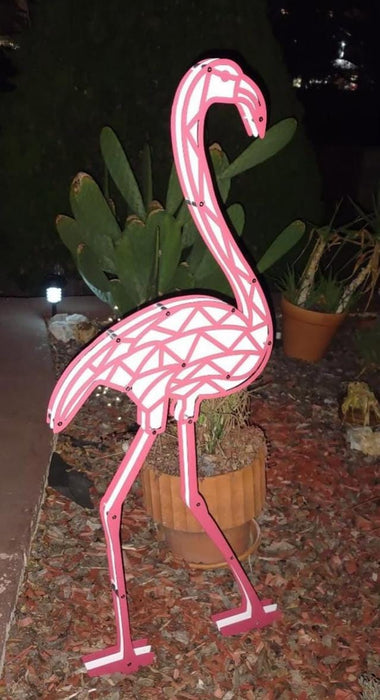 Pink flamingo-shaped neon light in a garden setting with plants and mulch.
