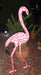 Pink flamingo-shaped neon light in a garden setting with plants and mulch.