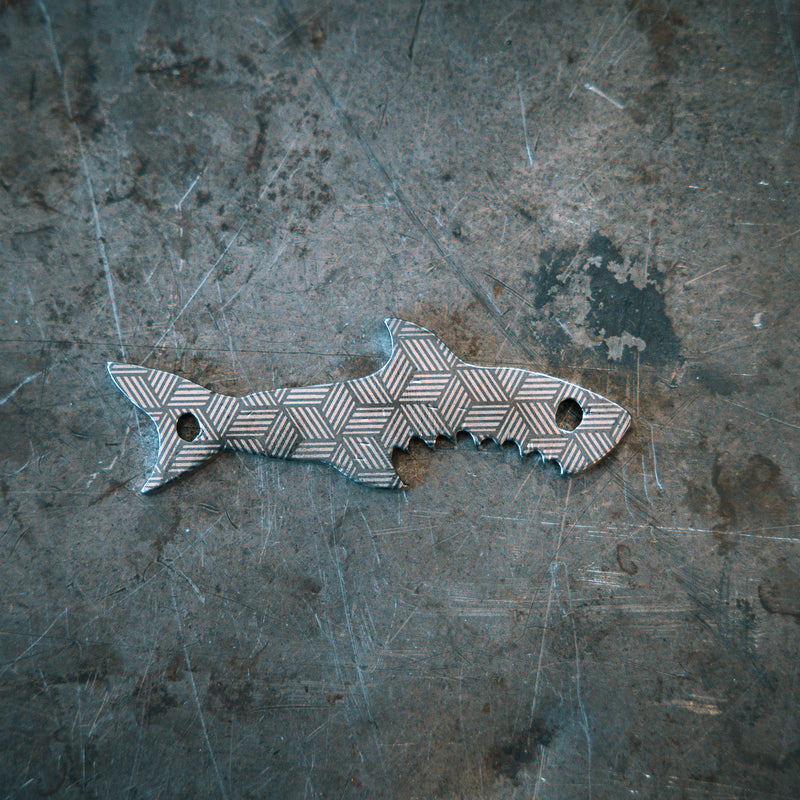 Decorative bottle opener shaped like a shark on a textured metal surface