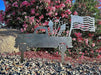 Decorative metal sculpture of a truck, horse, and flag in front of pink flowers