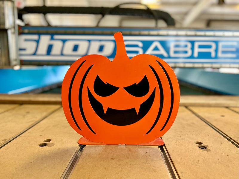 Individual shot of an orange powder-coated metal pumpkin with a sinister expression, featuring slanted angry eyes and a jagged toothy mouth.